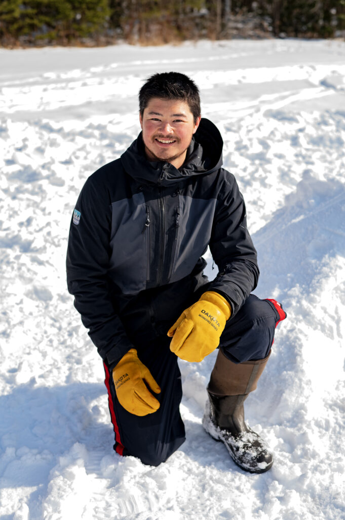 Mr. Fong kneeling in the snow beside a quinze
