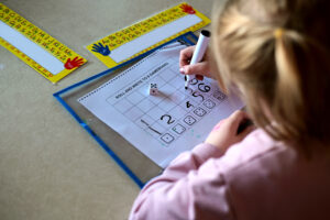 A girl plays one of the math games involving rolling a dice and then writing the number down on a grid