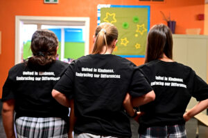 Students show the back of their shirts that say "United in kindness, embracing our differences"