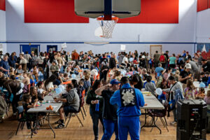 A full gymnasium of attendees in line for food as well as sitting at all the tables